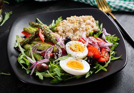 Photo for Breakfast oatmeal porridge with boiled egg, cherry tomatoes, asparagus and arugula. Healthy balanced food. - Royalty Free Image
