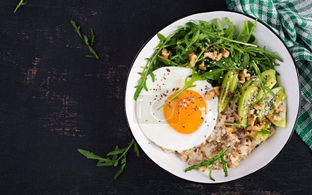 Foto de Desayuno gachas de avena con huevos asados, kiwi, rúcula y semillas de lino. Desayuno saludable para reducir el colesterol. Vista superior, plano - Imagen libre de derechos