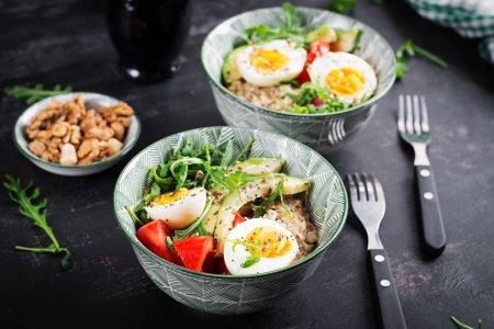 Breakfast oatmeal porridge with boiled eggs, avocado, tomatoes and green herbs. Healthy balanced food.
