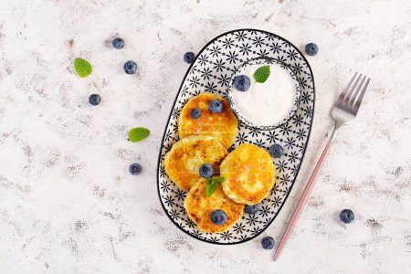 Photo for Cottage cheese pancakes with sour cream and blueberries on a light background. Breakfast or lunch. Top view - Royalty Free Image
