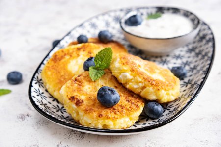Photo for Cottage cheese pancakes with sour cream and blueberries on a light background. Breakfast or lunch - Royalty Free Image
