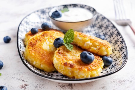 Photo for Cottage cheese pancakes with sour cream and blueberries on a light background. Breakfast or lunch - Royalty Free Image