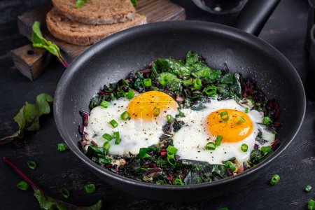 Photo for Breakfast. Fried eggs with green beet leaves, garlic, pepper and green onion in pan. - Royalty Free Image