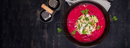Photo for Cold borscht, summer beet soup with fresh cucumber,  boiled egg and boiled chicken fillet on dark table. Traditional European food, delicious lunch. Top view, banner - Royalty Free Image