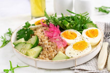 Photo for Breakfast oatmeal porridge with boiled eggs, cucumber, red onion and greens. Healthy balanced food. - Royalty Free Image