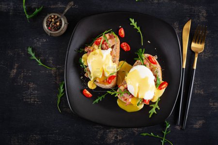 Photo for Breakfast. Sandwich with ham, poached egg, onion and arugula in a plate on a dark background. Top view - Royalty Free Image