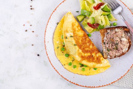 Photo for Omelette with green peas and toast with cod liver on white plate.  Frittata - italian omelet. Top view, flat lay - Royalty Free Image