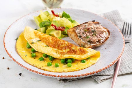 Photo for Omelette with green peas and toast with cod liver on white plate.  Frittata - italian omelet. - Royalty Free Image