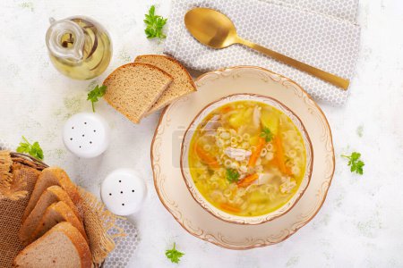 Foto de Sopa de pollo fresco con verduras y pasta stelline en un bol con zanahoria y perejil. Vista superior, plano - Imagen libre de derechos