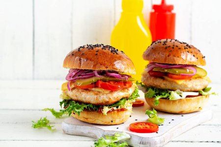 Foto de Hamburguesa de pollo. Sandwich con hamburguesa de pollo, tomates, queso, pepino en escabeche y lechuga. Hamburguesa con queso. - Imagen libre de derechos