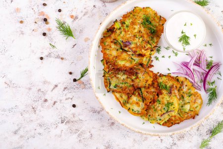 Photo for Zucchini fritters with red onions, garlic and herbs. Vegetarian zucchini pancakes and sour cream on white table. Top view - Royalty Free Image