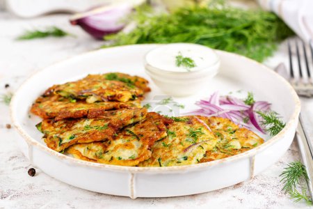 Photo for Zucchini fritters with red onions, garlic and herbs. Vegetarian zucchini pancakes and sour cream on white table. - Royalty Free Image