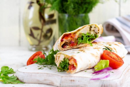Téléchargez les photos : Tortilla grillée enveloppe avec du poulet et des légumes frais sur une planche de bois blanc. Burrito au poulet. De la nourriture mexicaine. Concept d'alimentation saine. - en image libre de droit