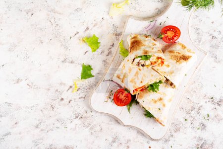Téléchargez les photos : Tortilla grillée enveloppe avec du poulet et des légumes frais sur une planche de bois blanc. Burrito au poulet. De la nourriture mexicaine. Concept d'alimentation saine. Vue du dessus - en image libre de droit