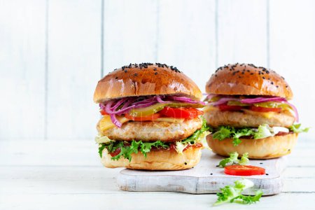 Foto de Hamburguesa de pollo. Sandwich con hamburguesa de pollo, tomates, queso, pepino en escabeche y lechuga. Hamburguesa con queso. - Imagen libre de derechos