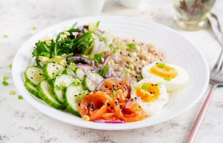 Photo for Breakfast oatmeal porridge with boiled eggs, salt salmon, cucumber and red onions. Healthy balanced food. Trendy food. - Royalty Free Image