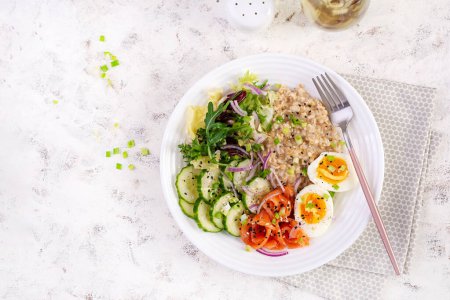 Photo for Breakfast oatmeal porridge with boiled eggs, salt salmon, cucumber and red onions. Healthy balanced food. Trendy food. Top view, flat lay - Royalty Free Image