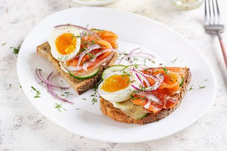 Photo for Delicious toast with salmon, boiled egg, cucumber and cream cheese on a white plate. Healthy eating, breakfast. Keto diet food. Tasty food. - Royalty Free Image