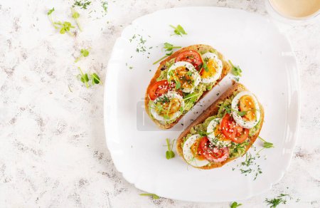 Photo for Delicious toast with avocado, boiled egg, tomatoes and microgreen on a white plate. Healthy eating, breakfast. Keto diet food. Trendy food. Top view - Royalty Free Image