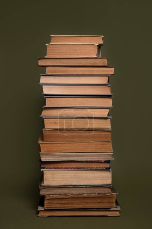 Foto de Una torre alta de libros antiguos que tienen páginas amarillentas, sobre un fondo verde oliva. - Imagen libre de derechos