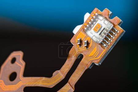 Photo for Closeup of optical sensor on electronic printed circuit board and flex ribbon cables on a dark blue background. Small orange die in transparent micro chip on PCB of dismantled digital CD/DVD disc drive. - Royalty Free Image