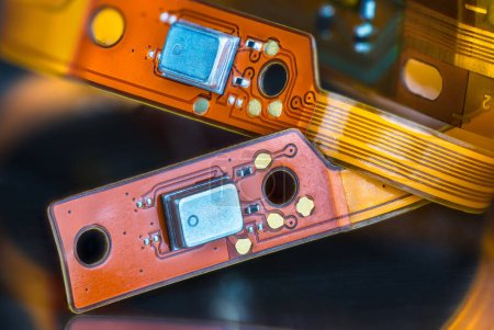 Schöne flexible elektronische Schaltungen auf gelben und orangefarbenen Streifen auf schwarzem, verschwommenem Hintergrund. Nahaufnahme von biegsamen Leiterplatten oder kleinen Komponenten auf flexiblen Flachbandkabeln aus dem Inneren von Kopfhörern.