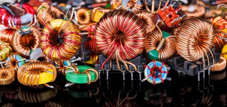 Photo for Closeup of colored inductors and transformers with reflection on a black background. Many toroidal coils with magnetic ferrite core wrapped in copper wire on electronic components pile. Electrotechnics. - Royalty Free Image