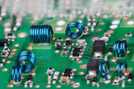 Photo for Blue air core inductors from metal wire on green printed circuit board of TV card RF module. Closeup a planar spiral coil and electronic components in PCB surface copper layer and bokeh in a background. - Royalty Free Image