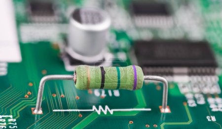 Photo for Closeup of resistor and white electronic symbol on a green PCB surface. Small component with color code and two metal wire terminals on printed circuit board and blurry capacitor or chips in background. - Royalty Free Image