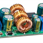 Electronic components on circuit board of power supply converter isolated on a white background. Close-up of toroidal coils, electrolytic capacitors or resistor trimmer and screw terminals on green PCB.