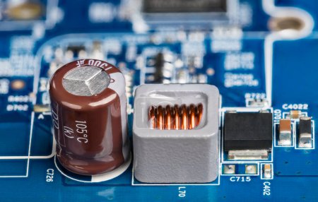 Foto de Primer plano del inductor, condensador electrolítico o transistor sobre fondo borroso de PCB. Placa de circuito impreso de fuente de alimentación azul con componentes electrónicos montados en superficie y condensador marrón o bobina gris. - Imagen libre de derechos