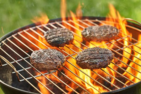 Foto de Grilling burgers on a charcoal grill in backyard cookout - Imagen libre de derechos
