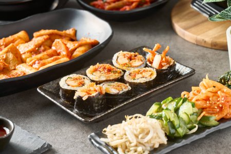 Téléchargez les photos : Rouleau de gimbap coréen avec calmar frit épicé sur assiette lors d'un grand dîner - en image libre de droit