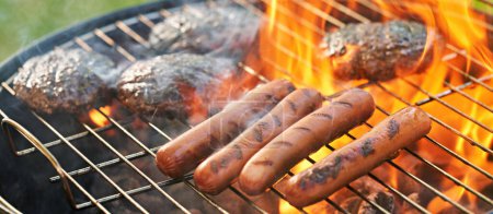 Foto de Grilling burgers and hot dogs on charcoal kettle grill outside in backyard - Imagen libre de derechos