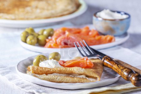 Pancakes with gravlax, cottage cheese and olives on a light background. A traditional dish for Maslenitsa or Carnival. Selective focus.