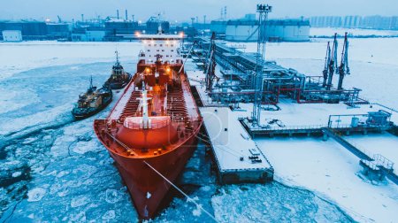 Oil shipment on big red tanker from terminal pumping system on water covered with thick layer of broken ice in frosty winter aerial view