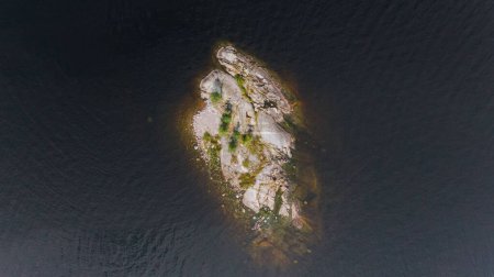 From above, an isolated rocky island with sparse vegetation stands out against the dark, rippling waters, creating a stark contrast and a sense of solitude in the vastness.
