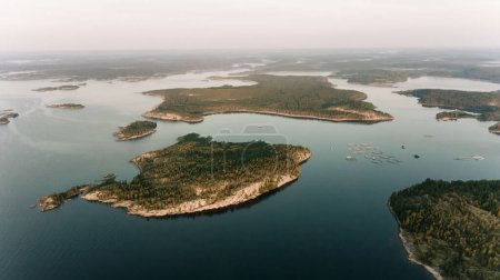 The soft light of dusk settles over a sprawling archipelago, where fish farms dot the tranquil waters between forested islands. The vastness of the scene emphasizes the harmony of industry and nature.
