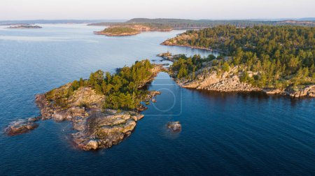 Vue aérienne de petites îles rocheuses avec forêt de conifères au milieu d'un grand lac en été à l'aube. Superbe paysage