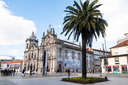 Téléchargez les photos : Une superbe église ornée de tuiles azulejo bleues traditionnelles se dresse à Porto, avec un palmier vibrant au premier plan d'une place animée. Portugal, Porto, janvier 2020. - en image libre de droit
