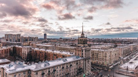 Die warmen Farbtöne der Abenddämmerung legen sich über ein schneebedecktes Stadtbild St. Petersburgs, wobei historische Architektur prominent vor einem dramatischen Himmel steht. Moskowski Prospekt in St. Petersburg.