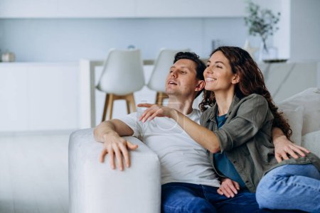 A relaxed couple lounges on a couch in a light-filled living room, sharing a moment of laughter and connection in a comfortable home setting