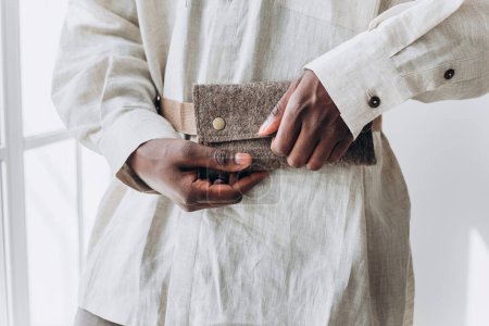 Close-Up of African American Mans Hands Holding a Textured Wallet. Close-up of a persons hands fastening a stylish felt wallet, showcasing a blend of practicality and fashion in soft natural