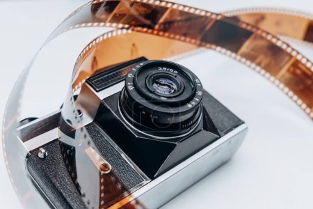 Una exhibición artística de una cámara vintage entrelazada con un carrete de película rizante, evocando nostalgia por la fotografía clásica y el cine.