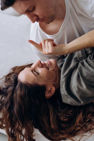 A joyful moment as a woman lying down laughs while playfully interacting with a man, highlighting a deep connection and shared happiness. Playful Couple Enjoying a Moment of Laughter and Connection