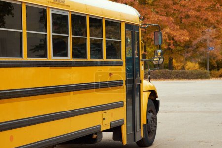 Foto de Autobús escolar amarillo se encuentra en el estacionamiento en el fondo del parque de otoño. - Imagen libre de derechos