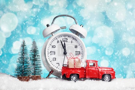 Téléchargez les photos : Camionnette jouet rouge avec un cadeau et un réveil blanc avec presque douze. Bonne année. - en image libre de droit