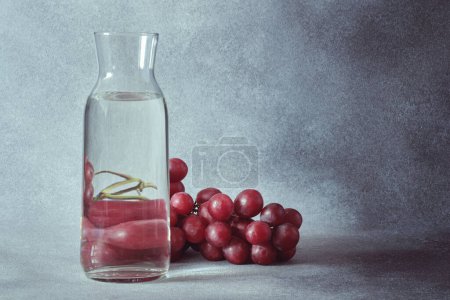 Téléchargez les photos : Carafe d'eau élégante avec raisins rouges sur fond gris texturé - en image libre de droit