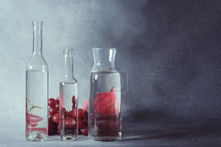 Téléchargez les photos : Nature morte des raisins vus à travers l'eau dans des bouteilles en verre clair - en image libre de droit