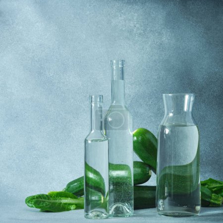 Photo for Glass water bottles and fresh green zucchini on a textured gray surface - Royalty Free Image